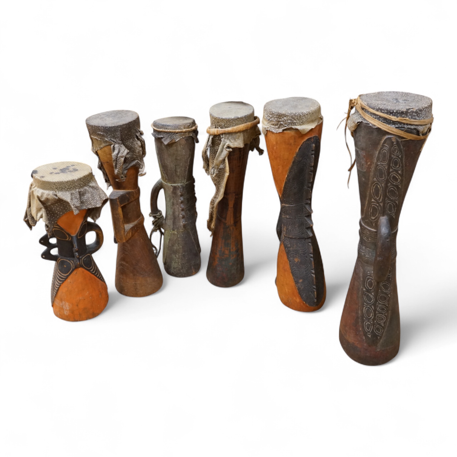 Six Papua New Guinea Sepik River Kundu wooden hand drums, of typical hour-glass form with skin tops, variously carved and incised with two painted, tallest 70cm